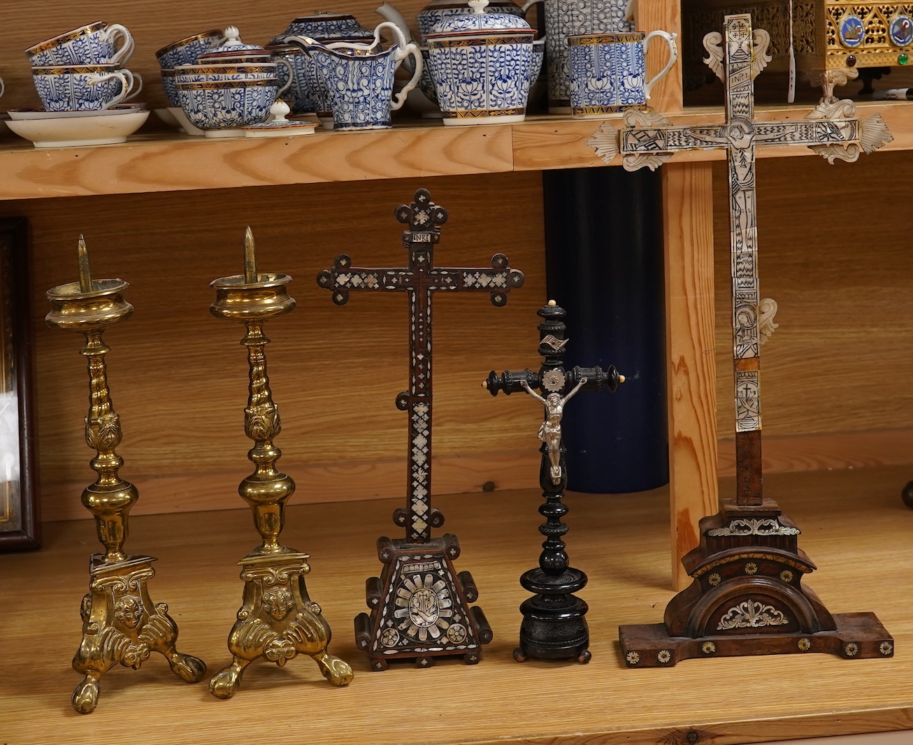 Two 19th century walnut and mother-of-pearl inlaid crucifixes and a German ebonised and white and metal mounted crucifix and a pair of Dutch or German brass tripod base cricket candlesticks, largest 56cm high (5)